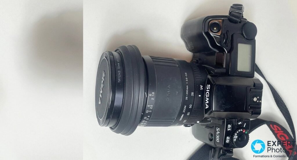 Sigma SA-300 avec son zoom 28-200 mm, marquage SA300 lisible sur le boîtier et filtre UV Tiffen 72 mm sur l'objectif 