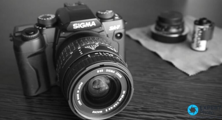 Sigma SA-7 noir avec zoom Sigma 28-80 mm f/3,5-5,6 monté, vue 3/4 avant en noir et blanc, cartouche Kodak en arrière-plan.