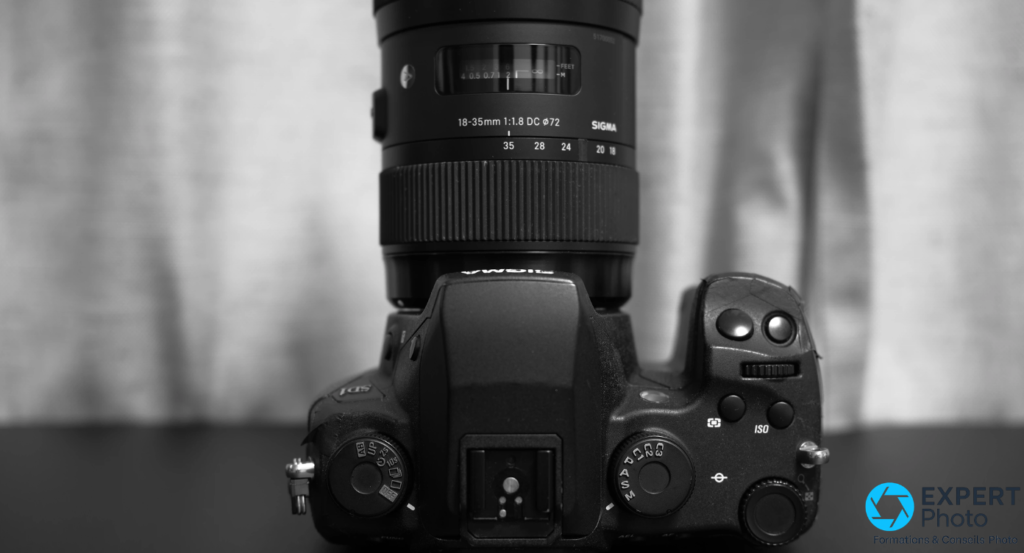 Vue de dessus du Sigma SD1 Merrill avec molette de modes P/A/S/M, accès direct ISO et objectif Sigma 18-35mm f/1.8 DC