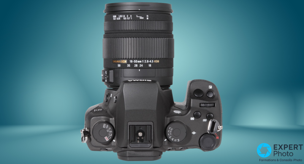 Vue de dessus du Sigma SD1 montrant la molette de modes, le sabot flash, les boutons ISO et AEL, et l'objectif 18-50mm