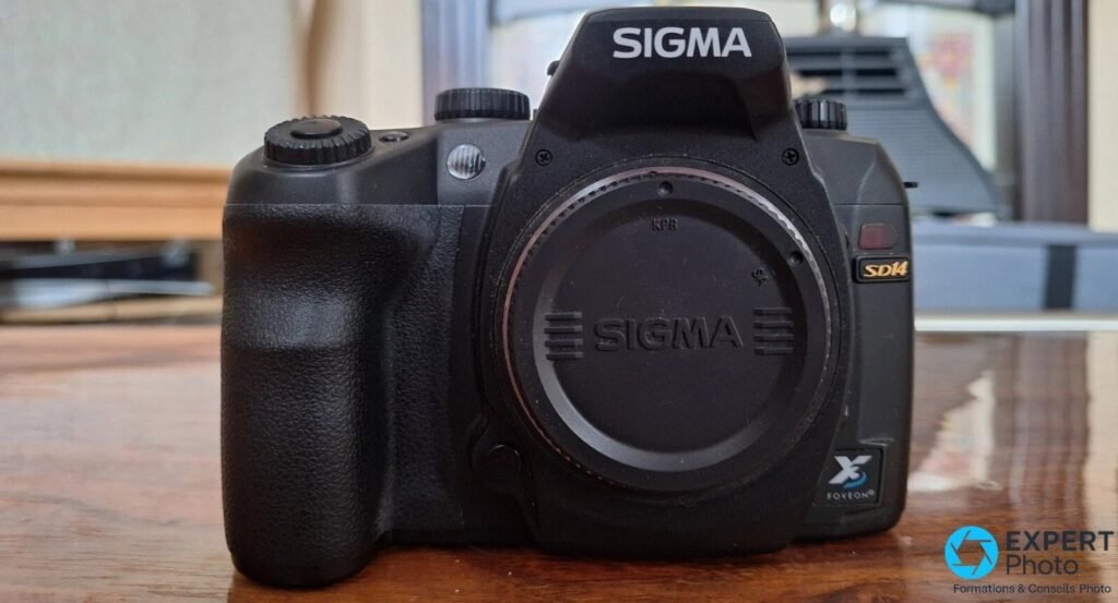Sigma SD14 noir vu de face, cache de monture Sigma installé sur la baïonnette, posé sur surface en bois en intérieur.