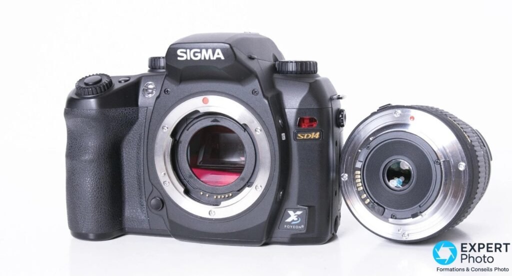 Sigma SD14 noir en vue trois quarts avant, monture ouverte capteur visible, optique zoom Sigma posée détachée à droite.