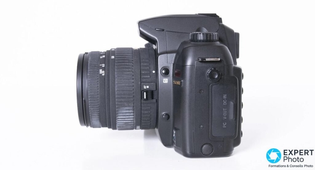 Sigma SD14 vu de profil gauche, objectif Sigma 18-50mm monté, trappe latérale fermée portant les inscriptions PC V-OUT DC-IN.