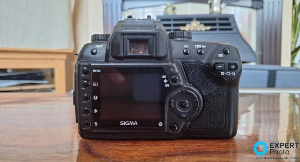 Sigma SD14 vu de dos, écran LCD 2,5 pouces éteint, boutons MENU et pavé directionnel, viseur optique en haut, table en bois.