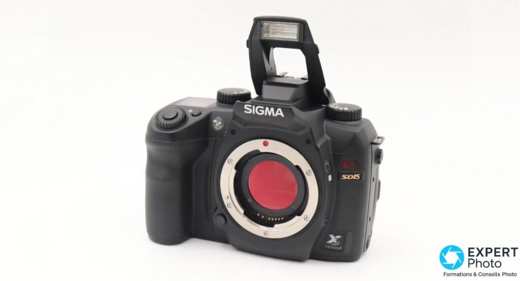 Sigma SD15 en trois-quarts avant, flash intégré pop-up relevé en position de tir, monture SA exposée.