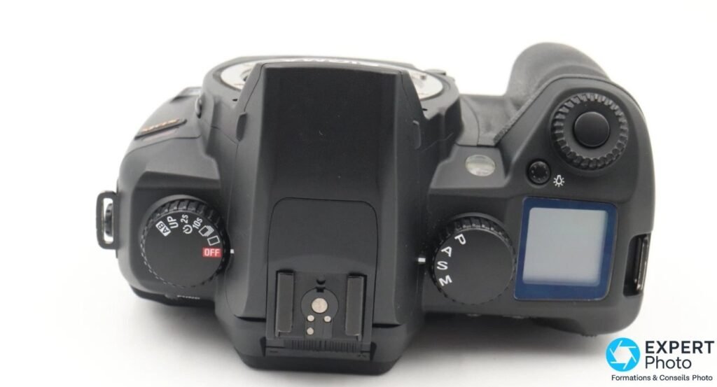 Sigma SD15 vu de dessus, griffe porte-flash centrale, molettes de modes P/A/S/M et entraînement, écran LCD secondaire.