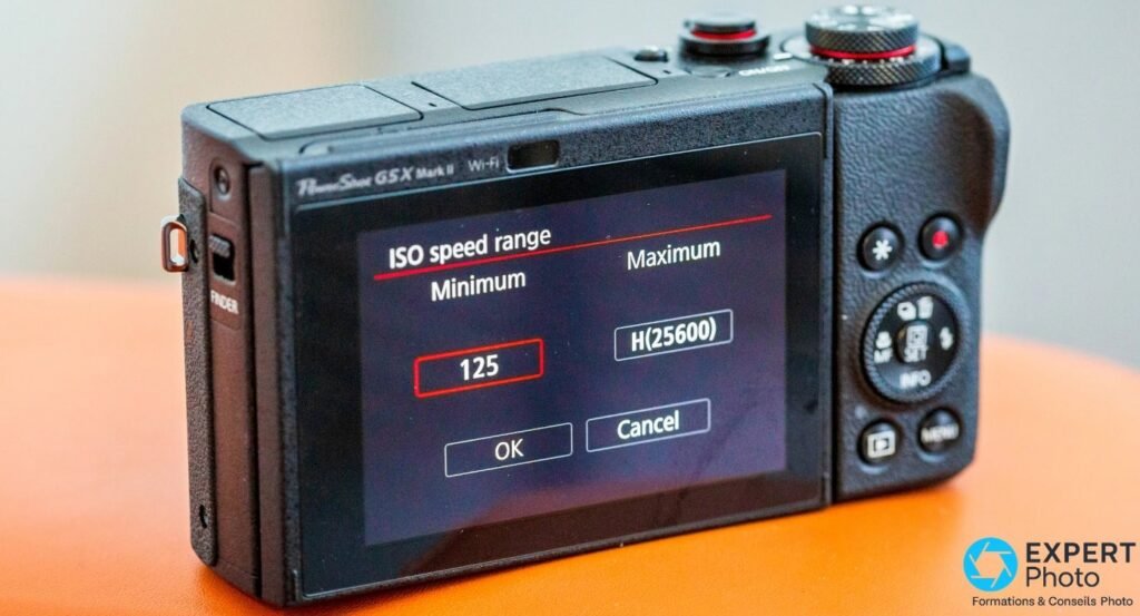 Canon G5 X Mark II vu de dos sur fond orange, écran affichant le menu ISO speed range Minimum 125 Maximum H.