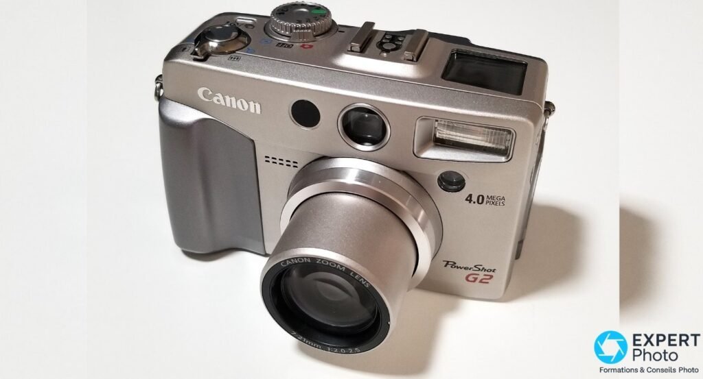 Canon PowerShot G2 argenté vu en trois quarts avant gauche, zoom Canon 7-21mm déployé, fond blanc neutre