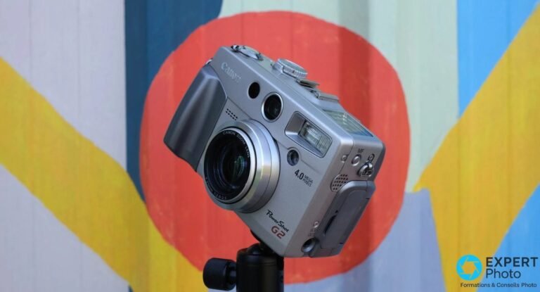 Canon PowerShot G2 monté sur trépied vu en trois quarts droit, fond mural extérieur peint, optique partiellement déployée