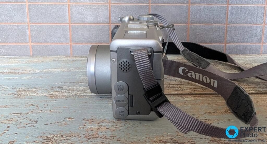 Canon PowerShot G3 vu de profil gauche avec ports DC IN 9.5V, DIGITAL et A/V OUT et sangle Canon dépliée.