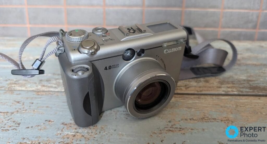 Canon PowerShot G3 vu de trois-quarts avant, objectif rétracté, mention 4.0 MEGA PIXELS et sangle dépliée à gauche.