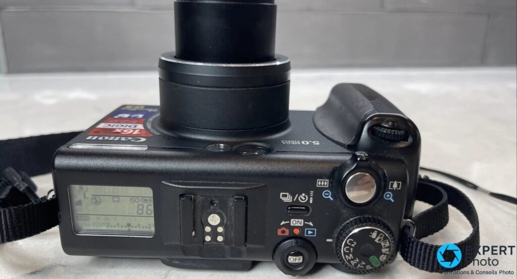 Canon PowerShot G5 vu de dessus, objectif déployé et écran LCD top affichant la sensibilité ISO et la balance des blancs. 