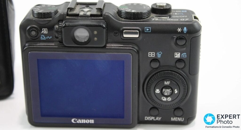 Canon PowerShot G7 vu de dos, écran LCD allumé bleu, viseur optique, pad MF FUNC.SET, boutons DISPLAY et MENU.