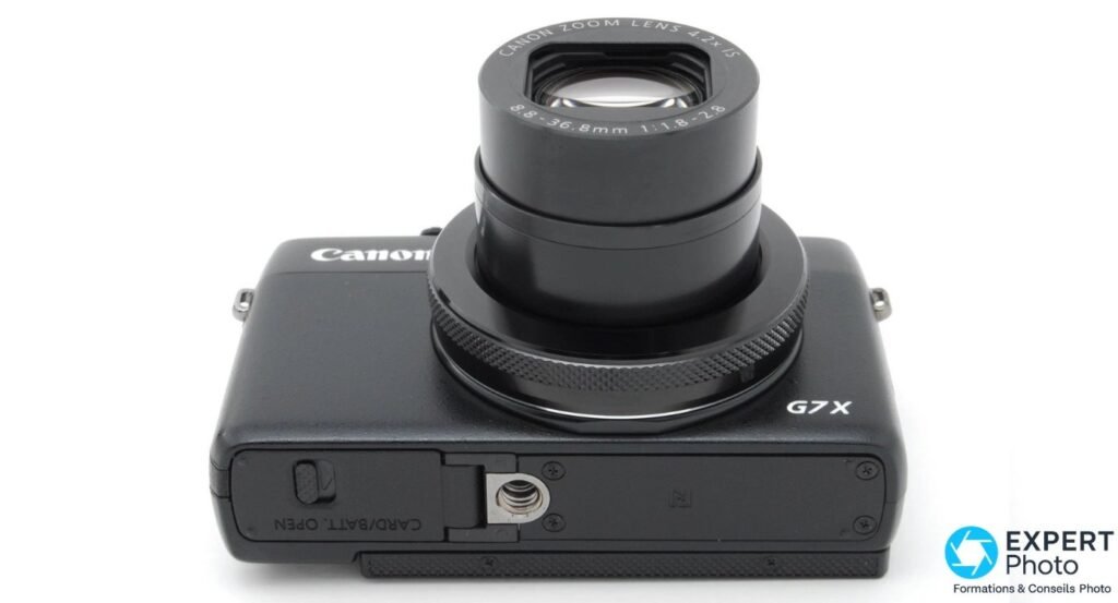 Canon PowerShot G7X de face, objectif déployé, mention G7X et trappe CARD/BATT OPEN visibles en bas