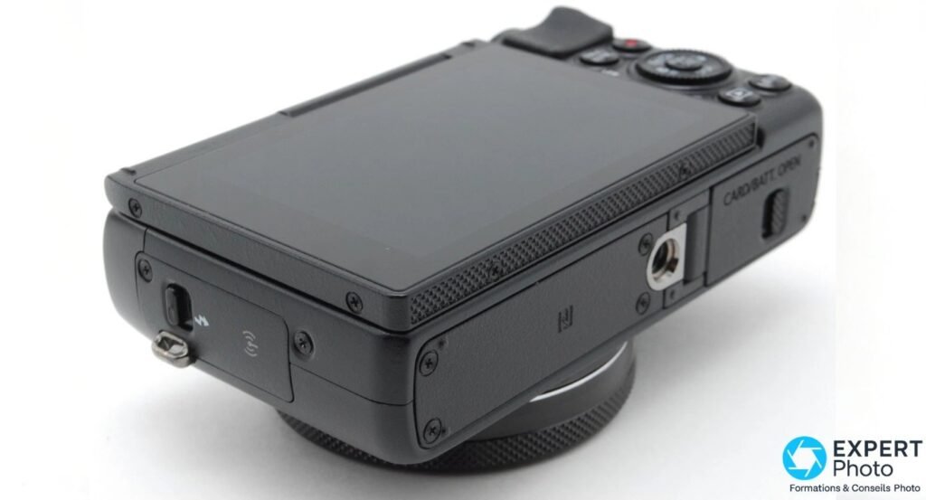Canon PowerShot G7X de trois-quarts arrière par-dessous, écran rabattu, filetage trépied et trappe NFC visibles