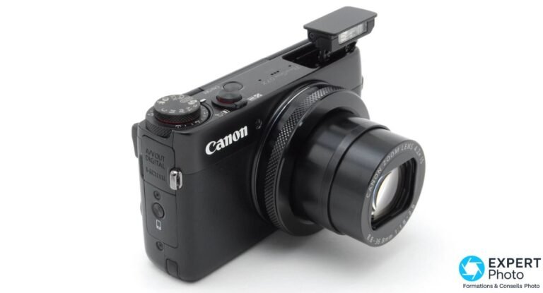 Canon PowerShot G7X en 2026 : Mark III, Mark II ou alternative ? Canon PowerShot G7X de trois-quarts avant, flash pop-up sorti, objectif télescopique déployé, posé sur fond blanc