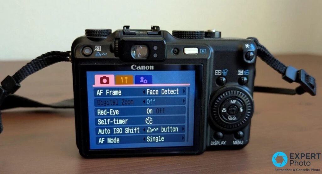 Canon PowerShot G9 vu de l'arrière, écran LCD allumé affichant le menu de réglages : AF Frame, Digital Zoom, Red-Eye.