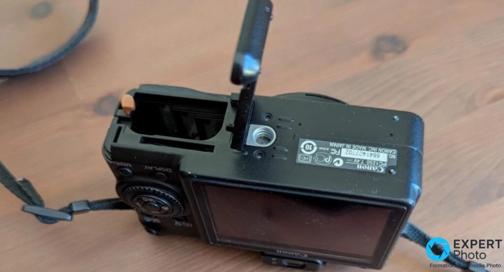 Canon PowerShot G9 vu de l'arrière, trappe à batterie ouverte, étiquette CANON PC1250 et filetage trépied visibles.