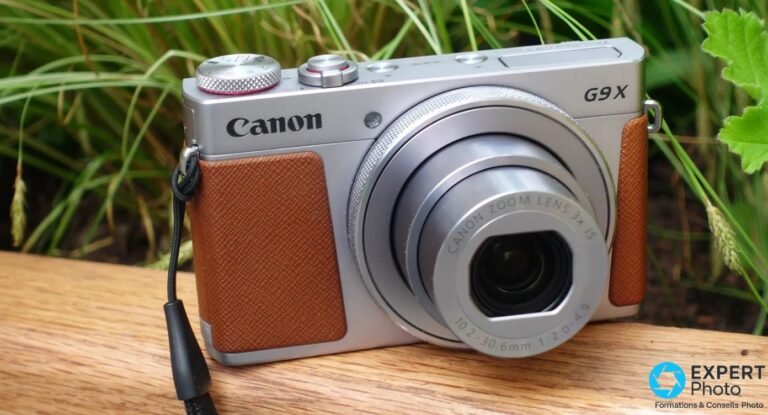 Canon PowerShot G9 X Mark II argenté avec grip cuir marron, zoom déployé, posé sur planche bois et fond d'herbes vertes.