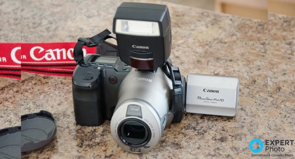 Canon PowerShot Pro70 vu de trois-quarts en plongée avec flash externe Canon sur la griffe et boîte d'origine.