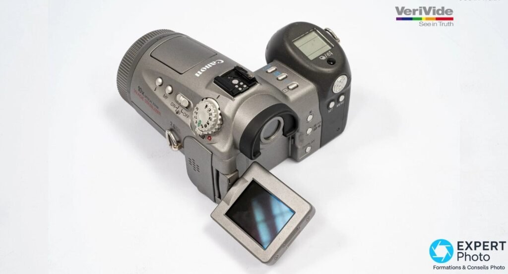 Canon PowerShot Pro90 IS, écran LCD orientable déployé vers l'avant, vue trois-quarts arrière, sabot et mode dial visibles.