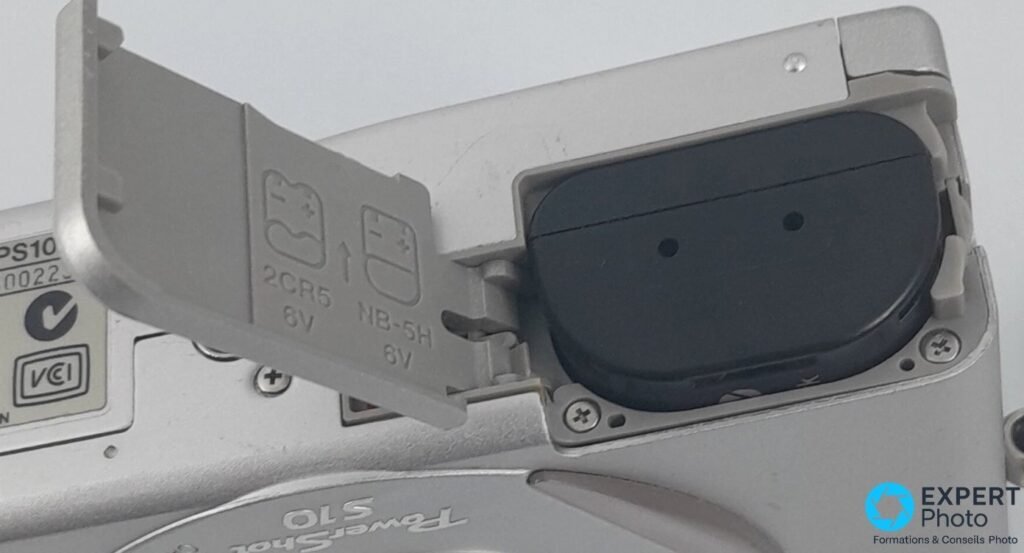 Canon PowerShot S10 — compartiment batterie ouvert, marquages 2CR5 6V et NB-5H 6V visibles sur la trappe.