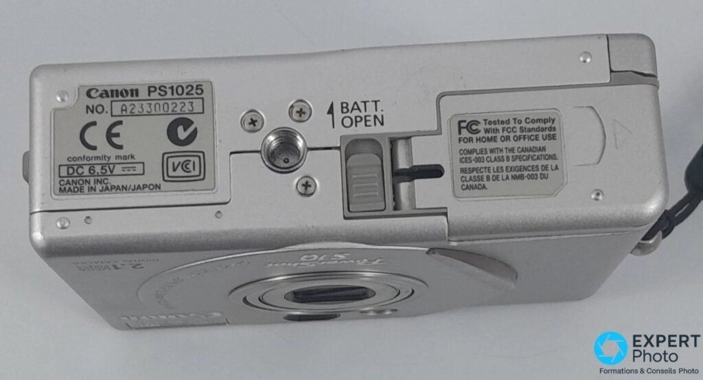 Canon PowerShot S10 vu de dessous, étiquette Canon PS1025, marquages CE et FCC, filetage trépied au centre. 