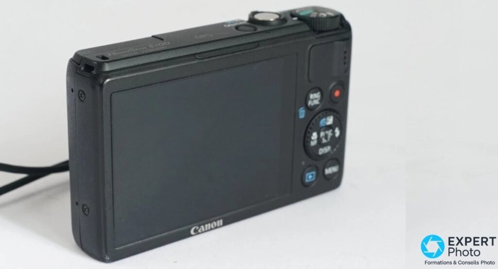 Canon PowerShot S100 vu de dos, écran LCD éteint, boutons RING FUNC, MENU et molette de navigation visibles.