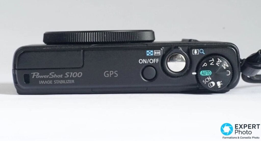 Vue de dessus du Canon PowerShot S100 avec molette de modes, bouton ON/OFF, marquage GPS et Image Stabilizer.