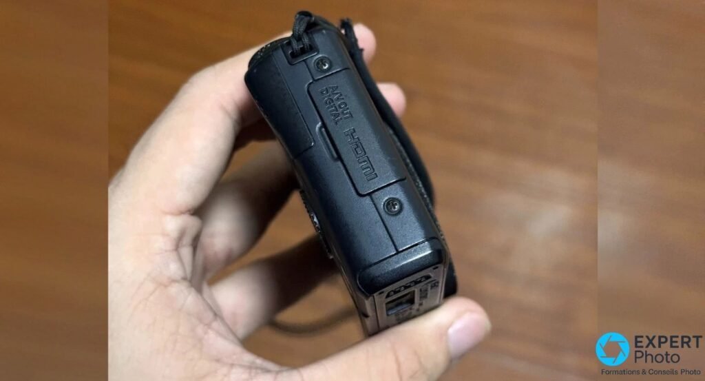Canon PowerShot S110 vu de profil, côté connectique avec cache marqué AV OUT DIGITAL et HDMI, deux passants de dragonne.