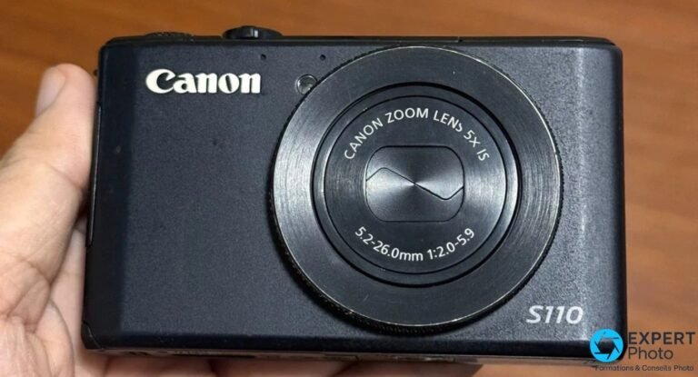 Test Canon PowerShot S110 : faut-il l’acheter d’occasion en 2026 ? Canon PowerShot S110 noir tenu en main, vue de face, objectif rétracté Canon Zoom Lens 5x IS 5,2-26 mm f/2-5,9, logo S110.