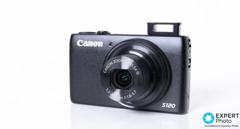 Canon PowerShot S120 noir vu de trois quarts avant, optique 5x IS sortie et flash pop-up relevé.