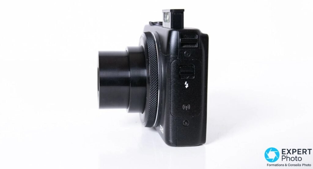 Profil du Canon PowerShot S120 avec optique sortie, flash relevé et pictogrammes flash/Wi-Fi visibles sur le flanc. 