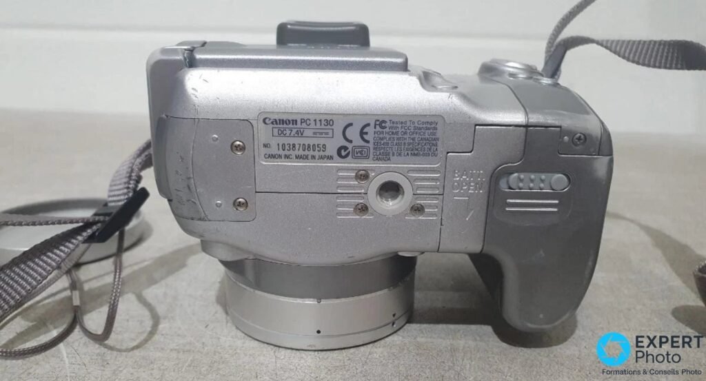 Canon PowerShot S2 IS vu de dessous, marquage Canon PC 1130, DC 7,4V, numéro de série, vis et trappe Batt Open visibles.
