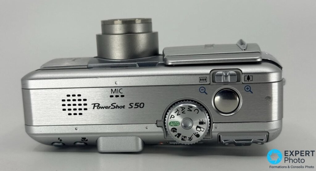 Canon PowerShot S50 vu de dessus, molette de modes AUTO/P/Tv/Av/M/C visible, déclencheur, levier de zoom et microphone.
