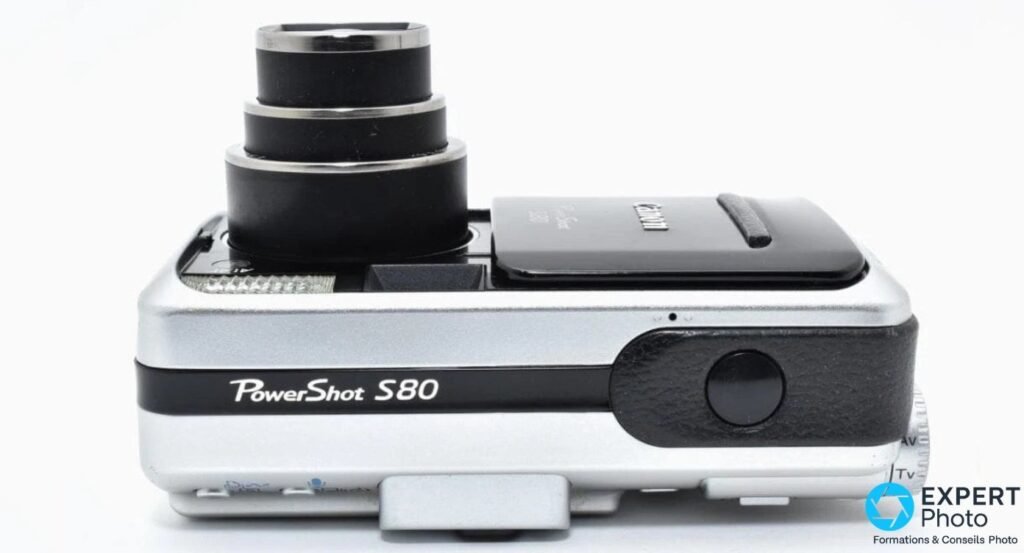 Canon PowerShot S80 vu de profil avec logo et objectif zoom déployé en position télé verticale.