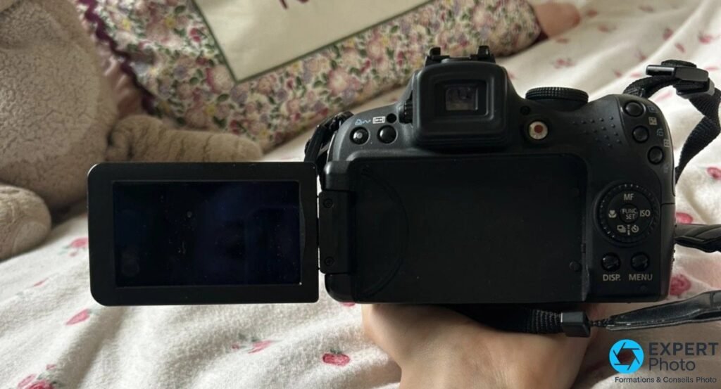 Canon SX1 IS vu de dos, écran LCD orientable déployé latéralement, viseur électronique et molette MF/FUNC/ISO visibles.