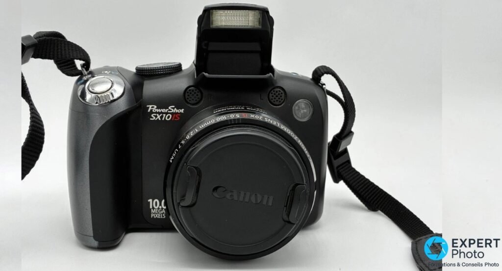 Canon PowerShot SX10 IS face avant, flash interne pop-up sorti, bouchon Canon, mention « PowerShot SX10 IS 10.0 Mpx »