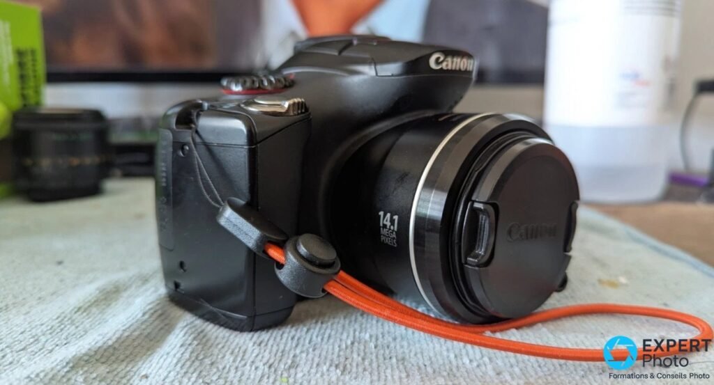 Canon PowerShot SX30 IS de trois quarts face droite, optique rétractée avec capuchon Canon, marquage 14.1 mégapixels lisible.