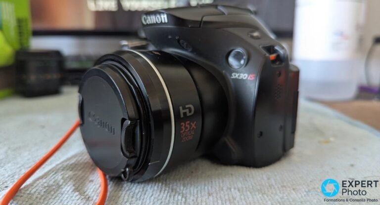 Test Canon PowerShot SX30 IS : que vaut ce bridge 35× en occasion ? Canon PowerShot SX30 IS de trois quarts face gauche, marquage HD 35× OPTICAL ZOOM en rouge sur le flanc de l'objectif.