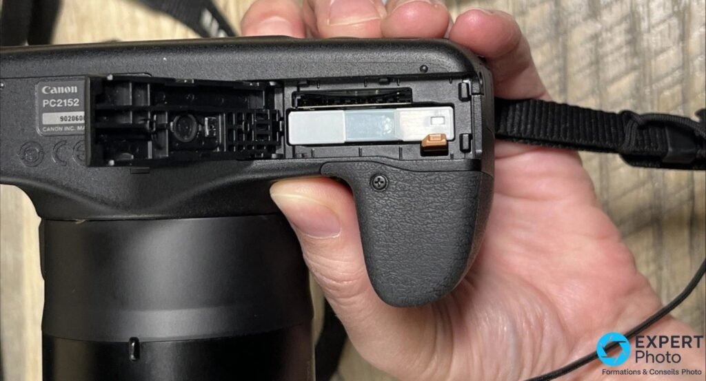 Compartiment batterie et carte SD ouvert sur Canon PowerShot SX520 HS, étiquette PC2152, carte mémoire engagée.