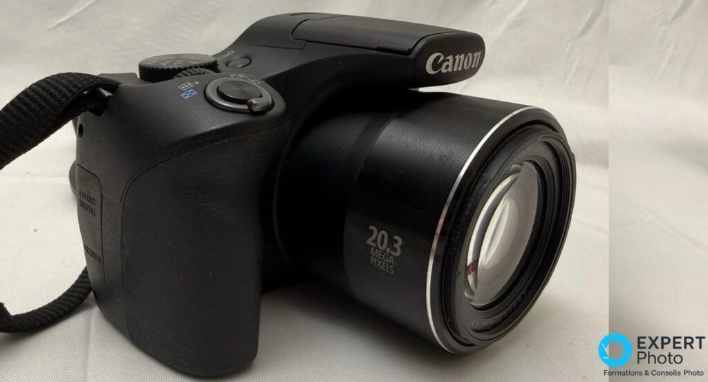 Canon PowerShot SX540 HS vu du côté gauche, marquage 20.3 MEGA PIXELS sur l'objectif et trappe A/V OUT DIGITAL visible.