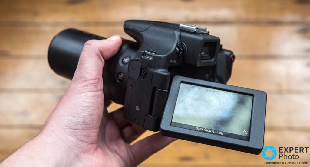 Écran orientable du Canon PowerShot SX60 HS déployé et retourné face avant, port MIC, NFC et Wi-Fi visibles