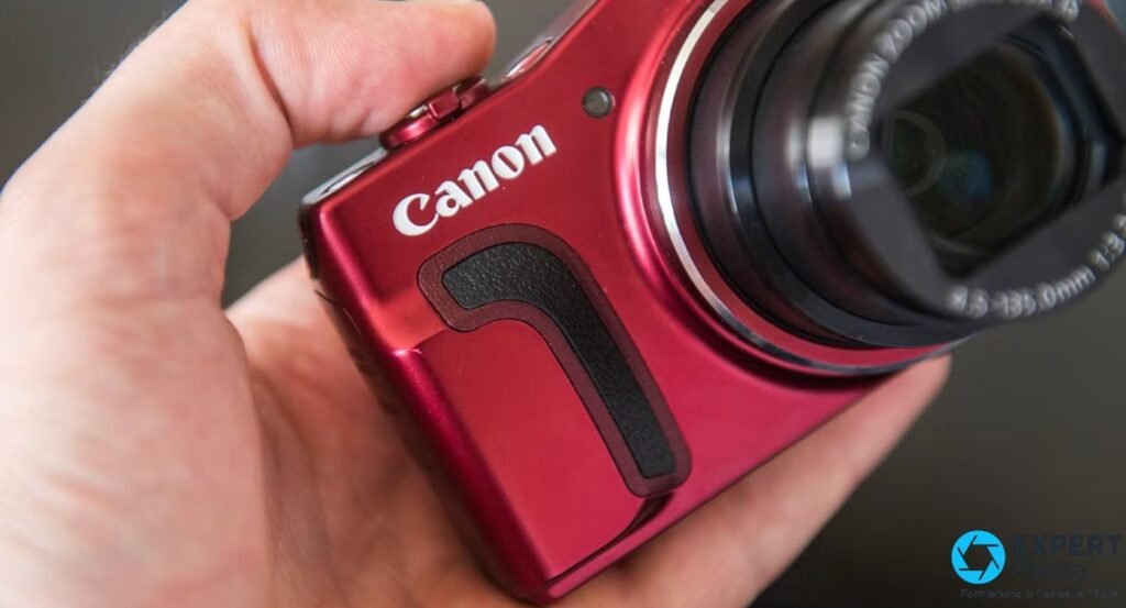 Gros plan sur le Canon PowerShot SX700 HS rouge tenu en main, grip noir en relief et logo Canon visibles.