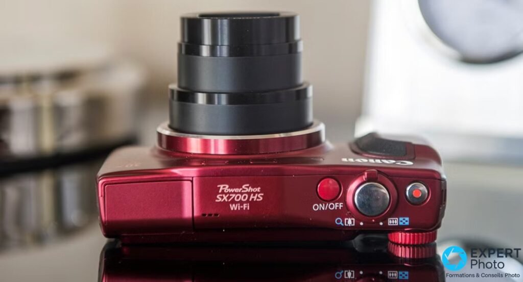 Canon PowerShot SX700 HS rouge posé vu de dessus, zoom optique 30x déployé, marquage PowerShot SX700 HS Wi-Fi visible.