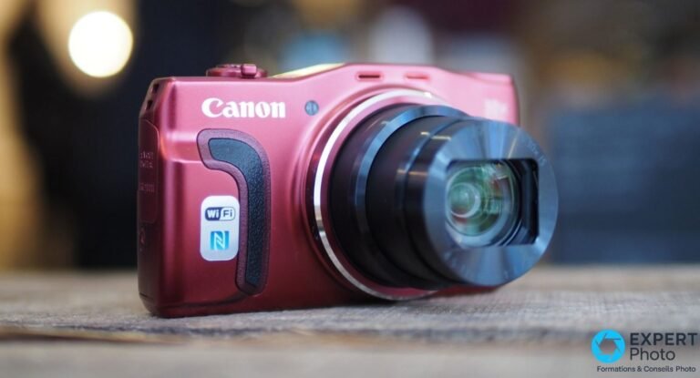 Canon PowerShot SX710 HS rouge en vue 3/4 avant, zoom optique 30x entièrement déployé, posé sur un plan en bois.