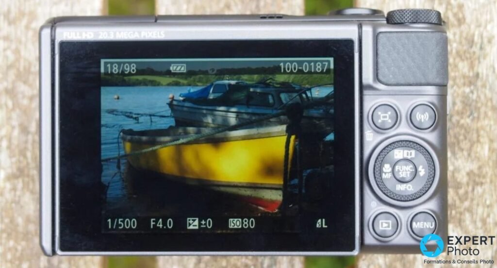 Canon PowerShot SX730 HS face arrière silver, écran allumé sur photo de bateau, boutons physiques et molette visibles. 