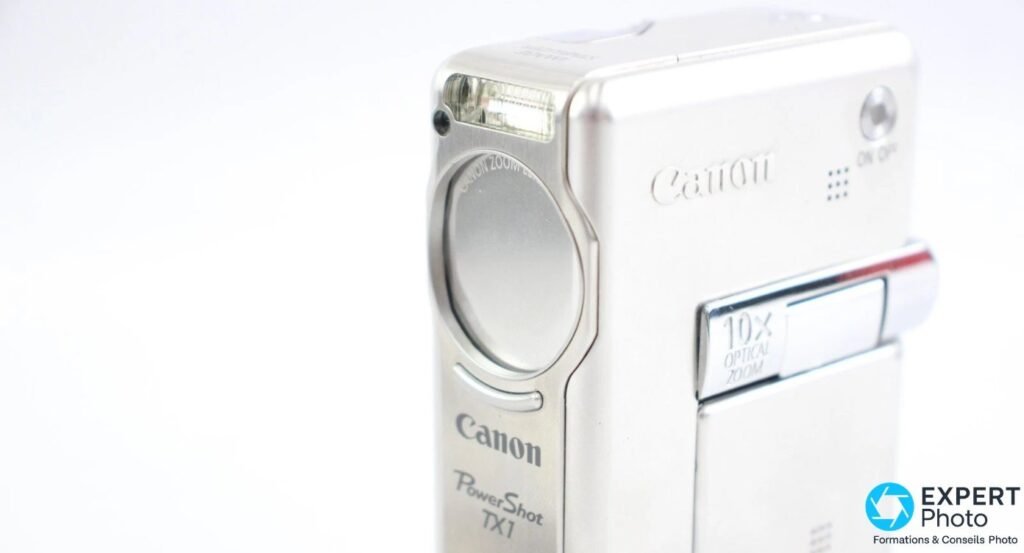 Canon PowerShot TX1 silver vu de face en 3/4 droit avec marquages Canon, PowerShot TX1 et 10x optical zoom