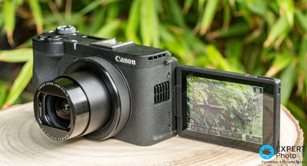 Canon PowerShot V1 vu de trois quarts avant, écran orientable déployé sur le côté droit, objectif déployé. 