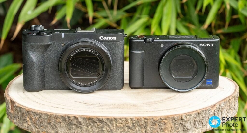 Canon PowerShot V1 (gauche, objectif déployé) et compact Sony à objectif Zeiss (droite) sur une rondelle de bois.